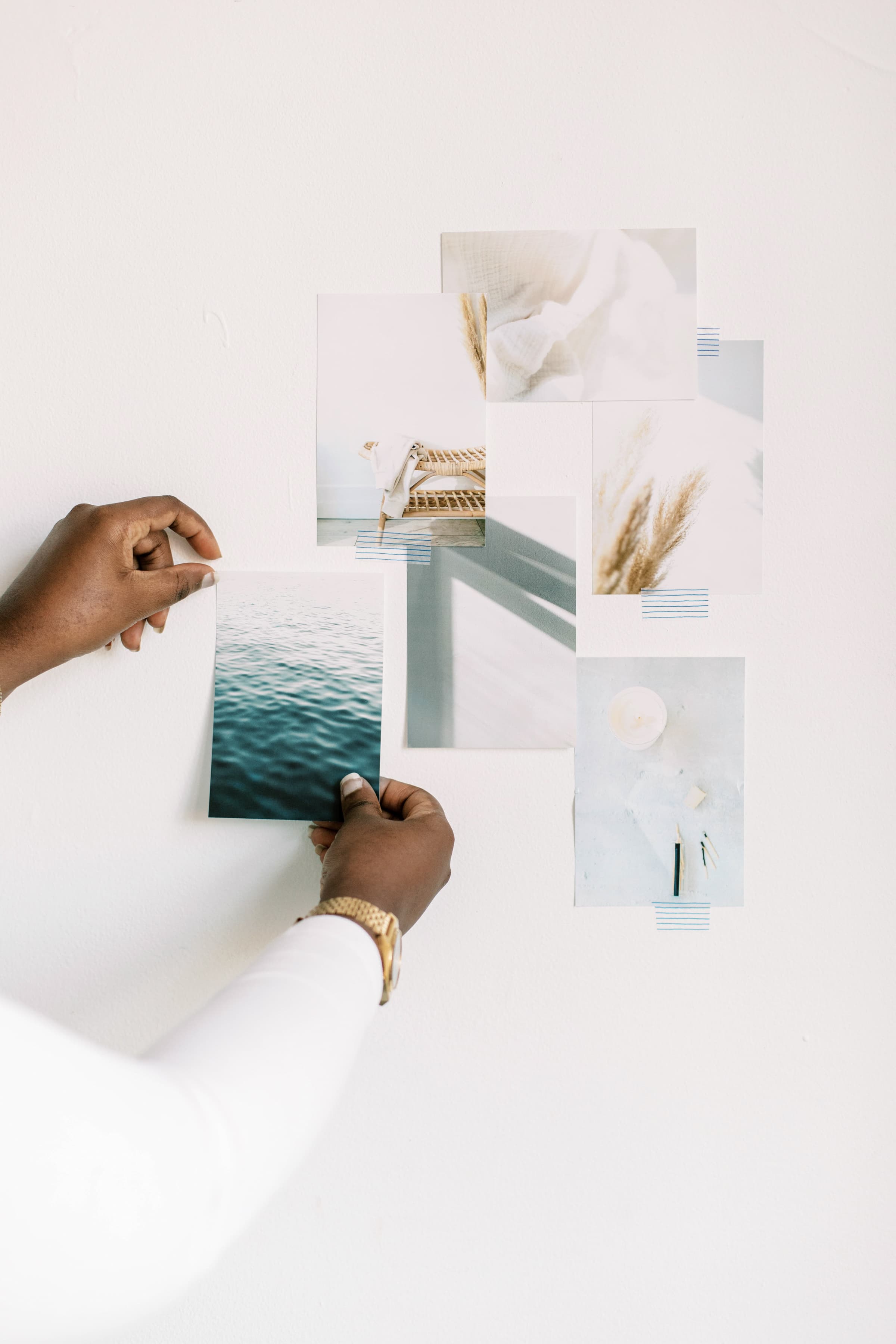 A woman in a white shirt wearing a gold watch pins items to a vision board.